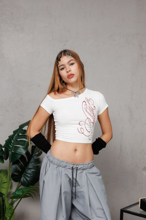 Top off shoulder Bellakita CHILL blanco cropped — algodón spandex con manga asimétrica y lettering script en serigrafía roja, top femenino streetwear hecho en Colombia